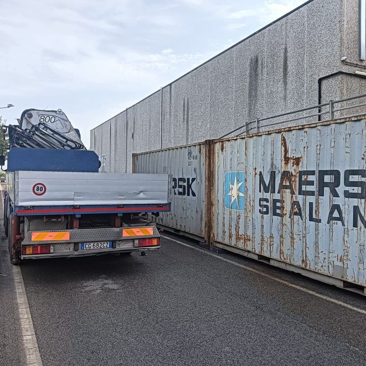Un netturbino con indosso un giubbotto ad alta visibilità svuota un cassonetto in un camion verde in strada.