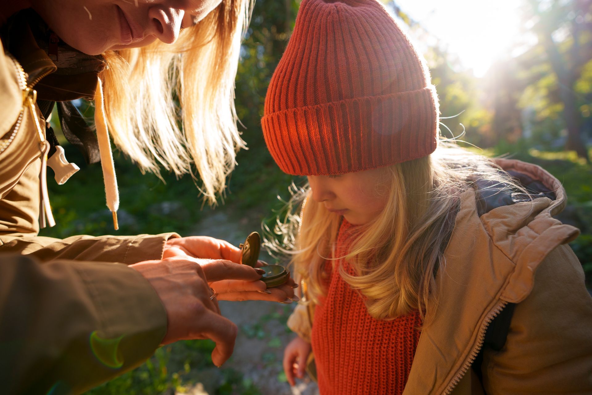 Woman and child examining something outdoors, sunlight. Child wears an orange hat and scarf.
