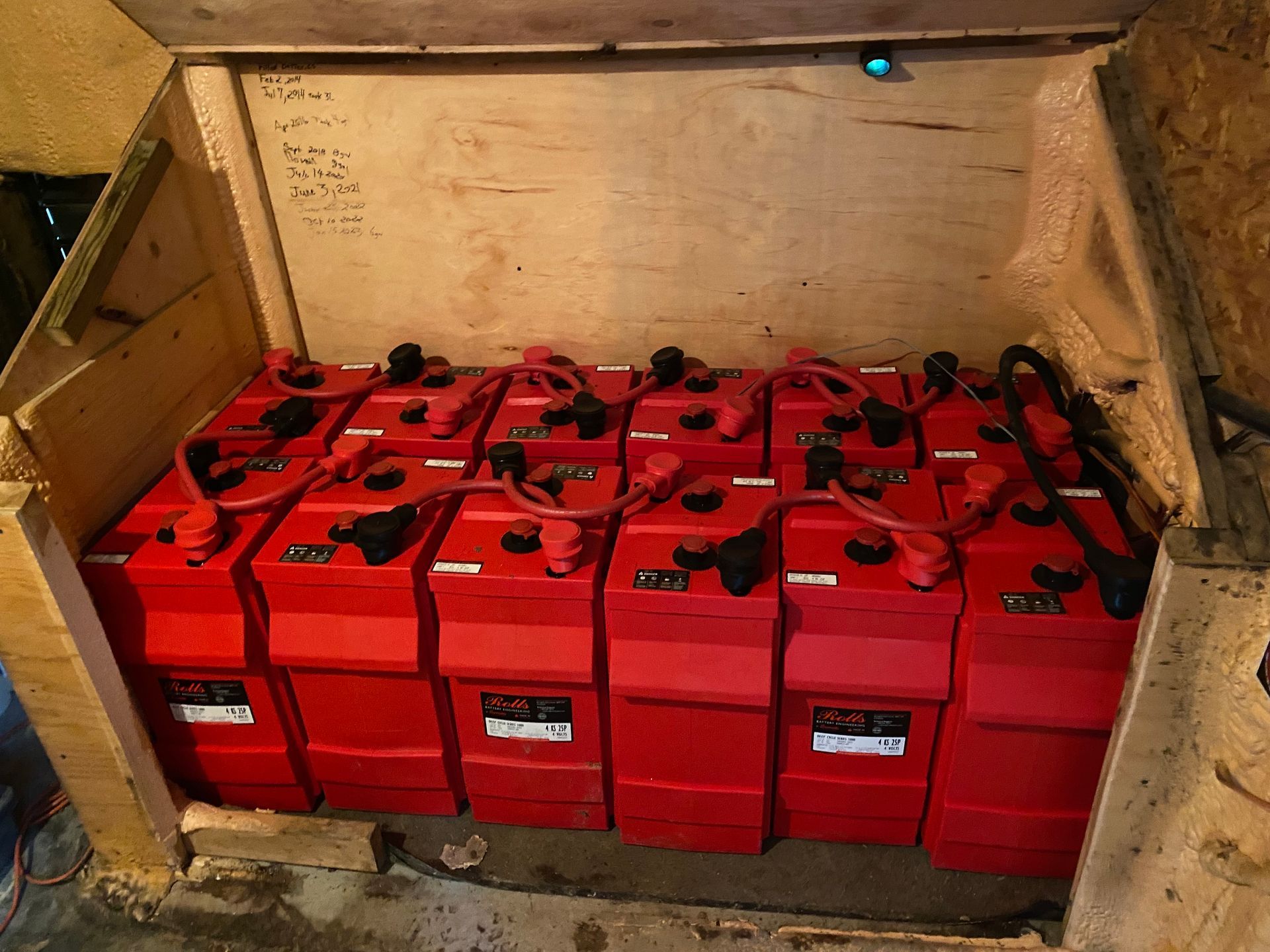 Red batteries inside a wooden enclosure, connected with black and red cables.