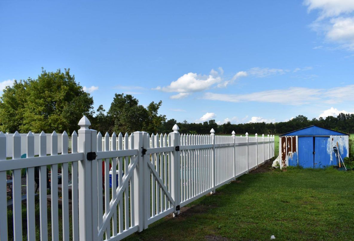 A white picket fence surrounds a grassy field with a blue tent in the background.
