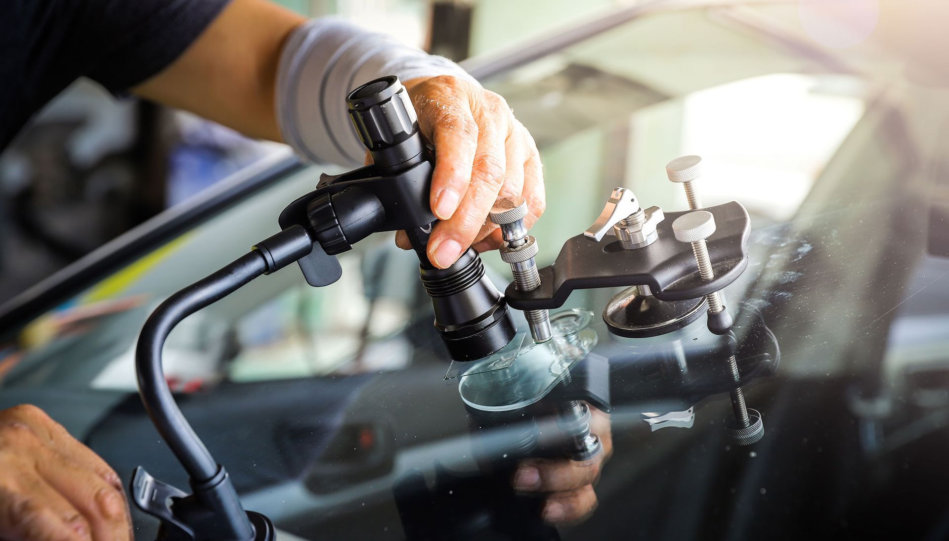 Person repairing windshield crack with specialized equipment in a garage.