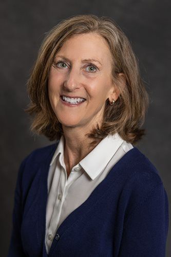 Portrait of a smiling person in a white shirt and navy sweater against a dark background