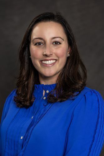 Portrait of a smiling woman in a bright blue blouse against a dark studio background