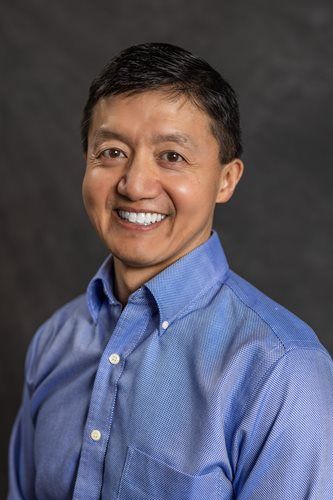 Smiling man in a blue button-down shirt against a dark gray background
