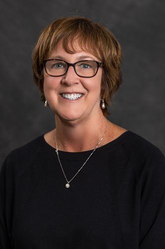 Smiling woman wearing glasses and a black top against a dark gray studio backdrop