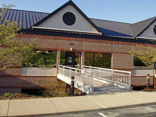Brick building entrance with white ramp railing, blue roof, and trees in front