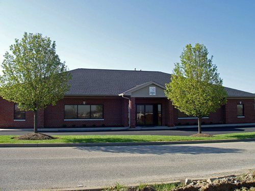 Brick commercial building with two trees and a road in front under a clear blue sky