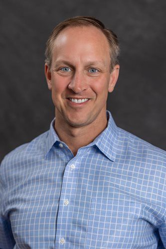 Portrait of a smiling man in a blue checkered shirt against a dark gray background