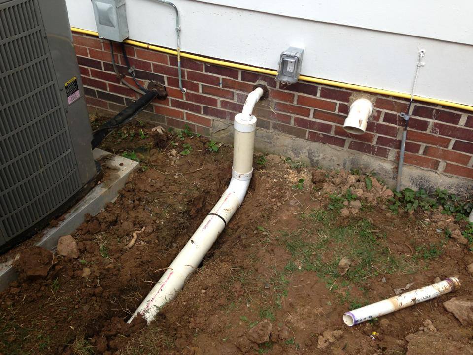 A white pipe is laying in the dirt next to a brick wall.