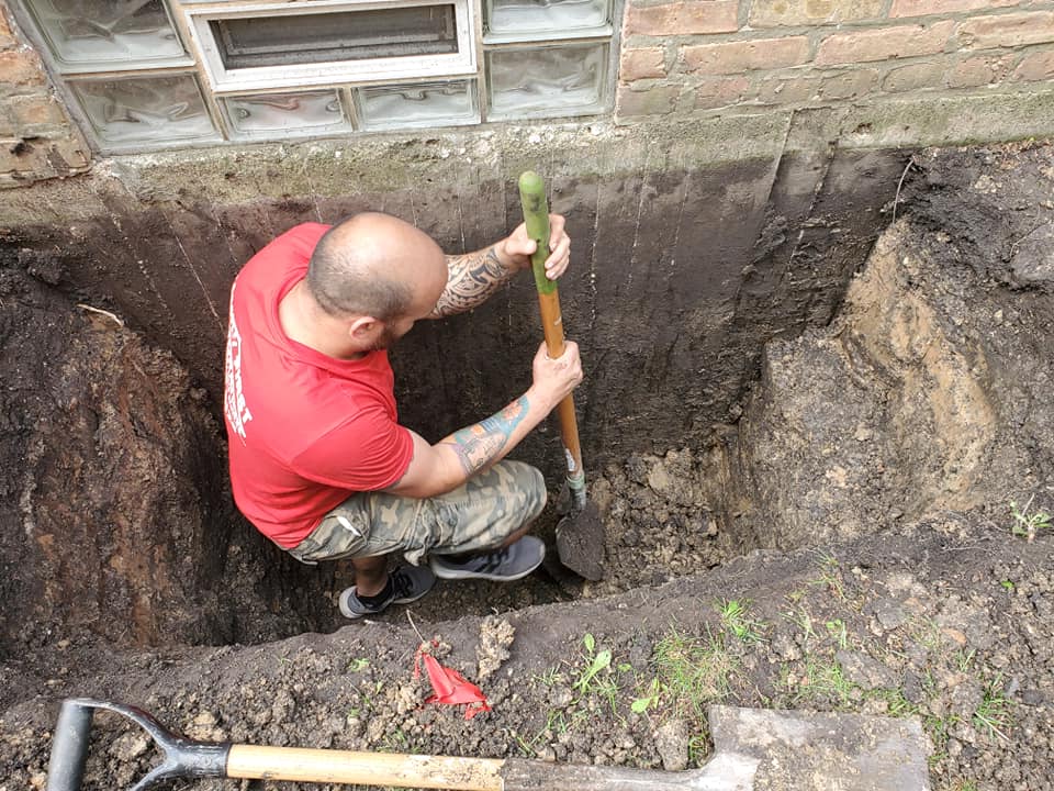 A man in a red shirt is digging a hole with a shovel.