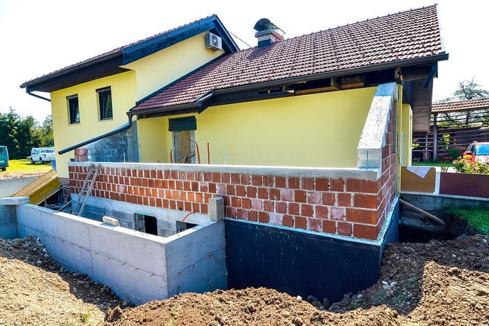 A yellow house is being built with a brick foundation.