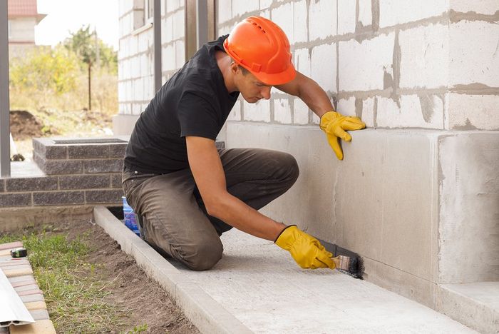 A man is kneeling down and painting a concrete wall.