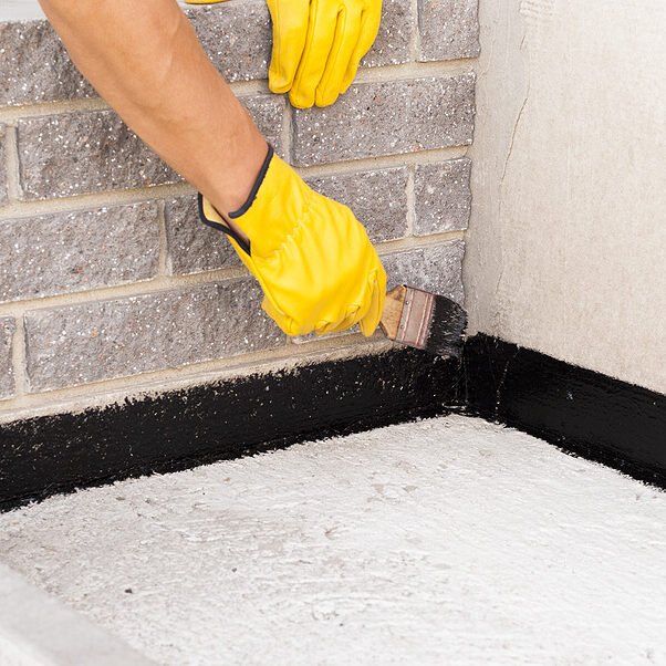 A person wearing yellow gloves is painting a brick wall