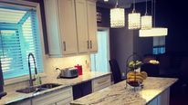 Bright modern kitchen with white cabinets, marble island, pendant lights, and a window over the sink.