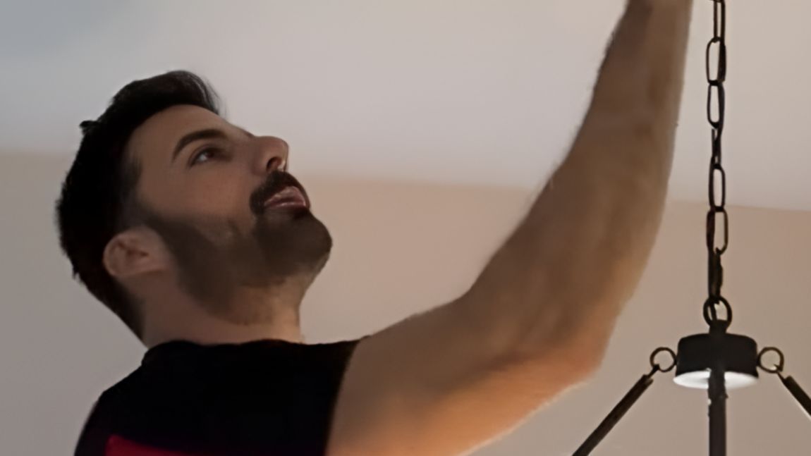Man in a black shirt reaching up toward a hanging chain indoors