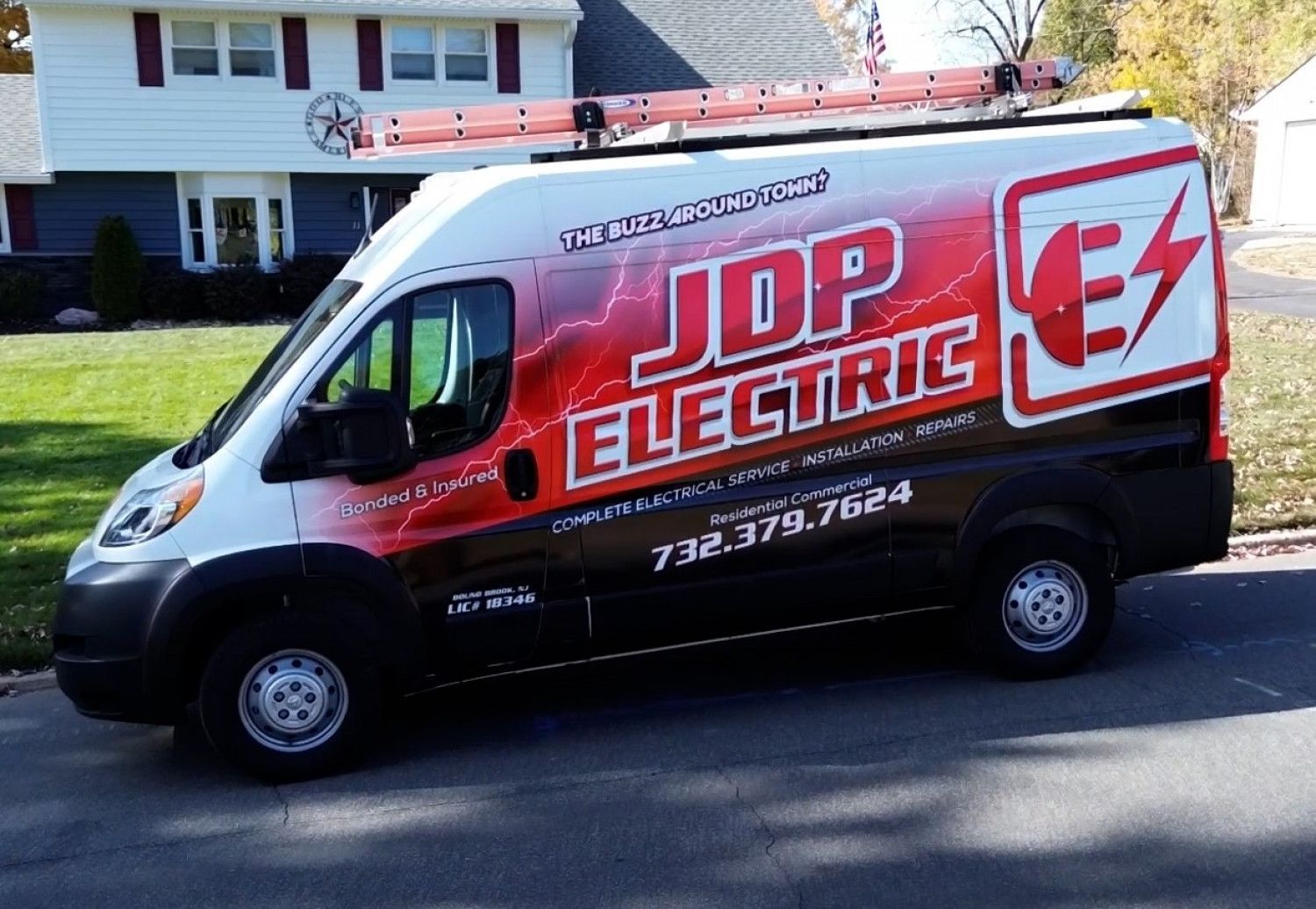 Red JDP Electric van parked on a residential street with a house in the background