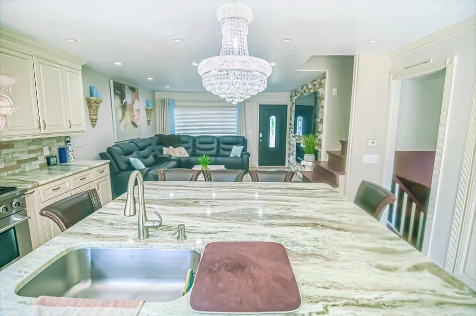 Bright kitchen with marble island, sink, chandelier, and teal sofa in adjacent living area