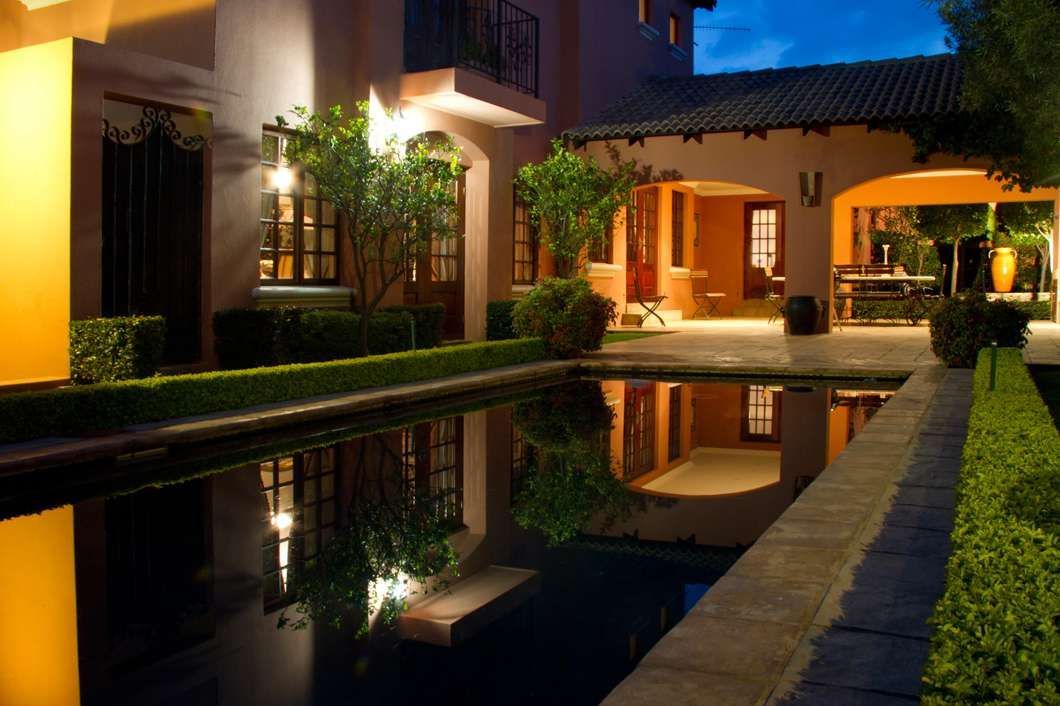 Luxurious villa courtyard at night with a lit pool and palm trees reflecting in the water