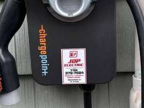 Close-up of a black ChargePoint EV charging station with a JPP Electric sticker and plugged-in cable