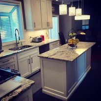 Modern kitchen with white cabinets, granite island, pendant lights, and a window over the sink