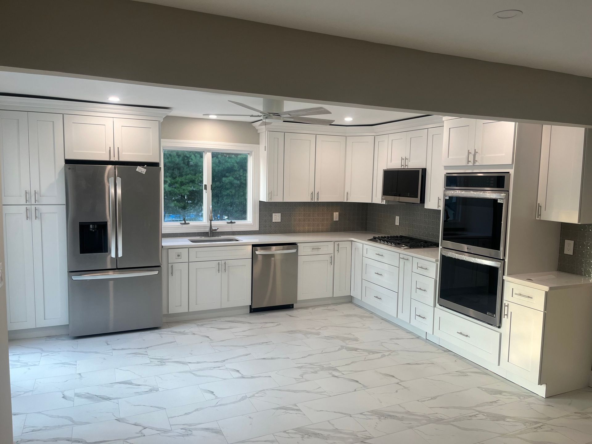Bright modern kitchen with white cabinets, stainless appliances, and marble-look flooring