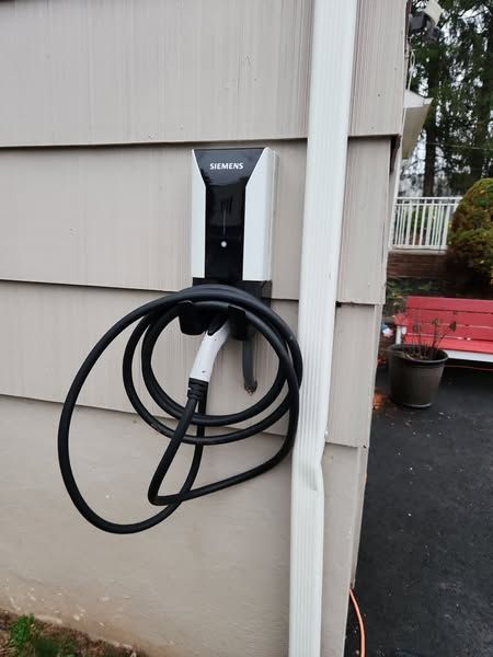Wall-mounted EV charger with coiled black cable on the side of a house