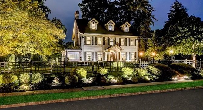 Illuminated white house at night with landscaped front yard and trees