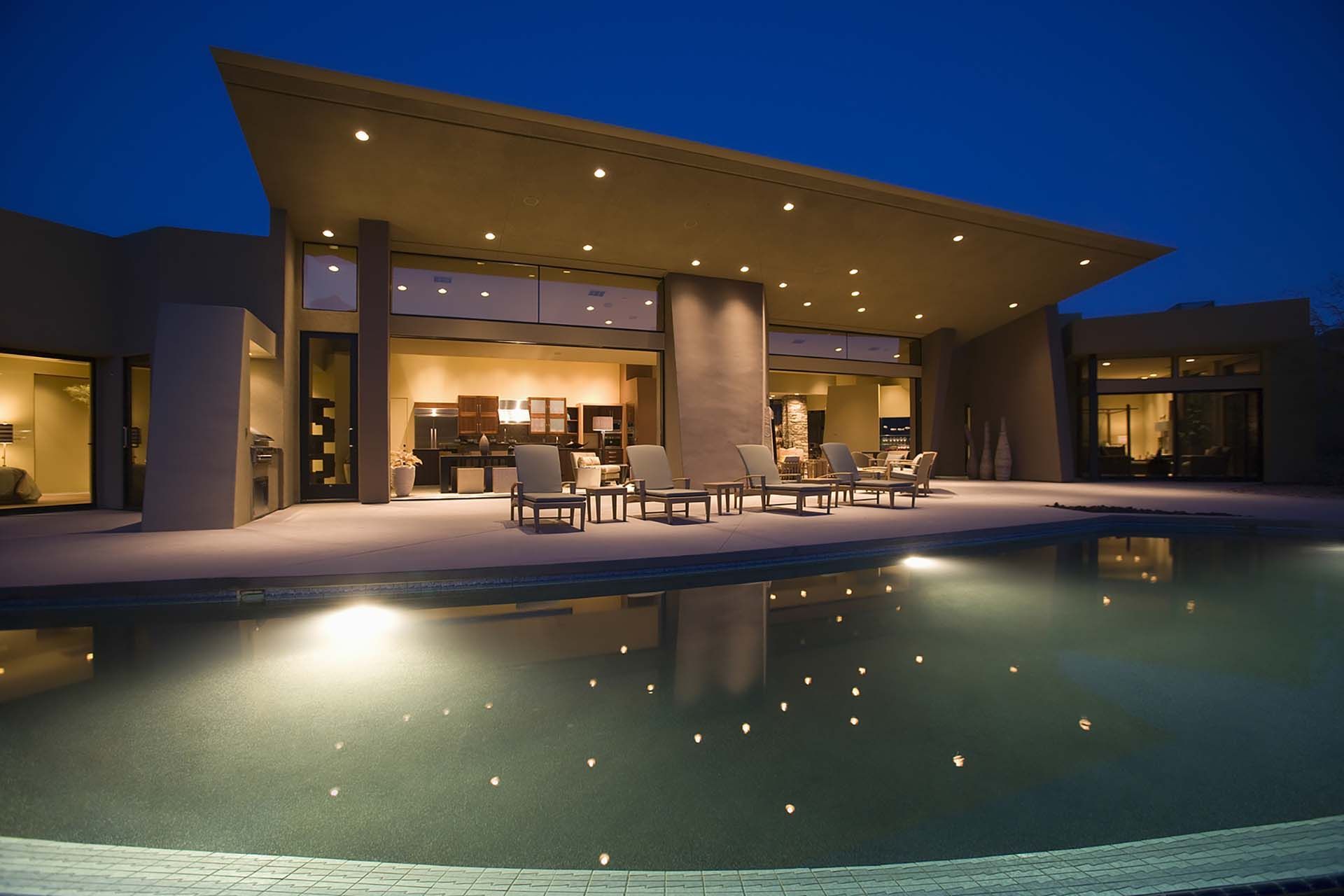 Modern luxury home at dusk with lit patio and reflection in a swimming pool