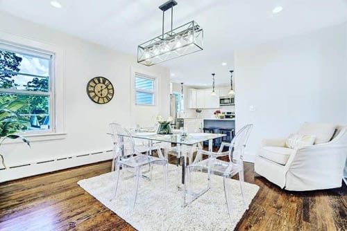 Bright white dining room with glass table, white chairs, hardwood floors, and a chandelier.