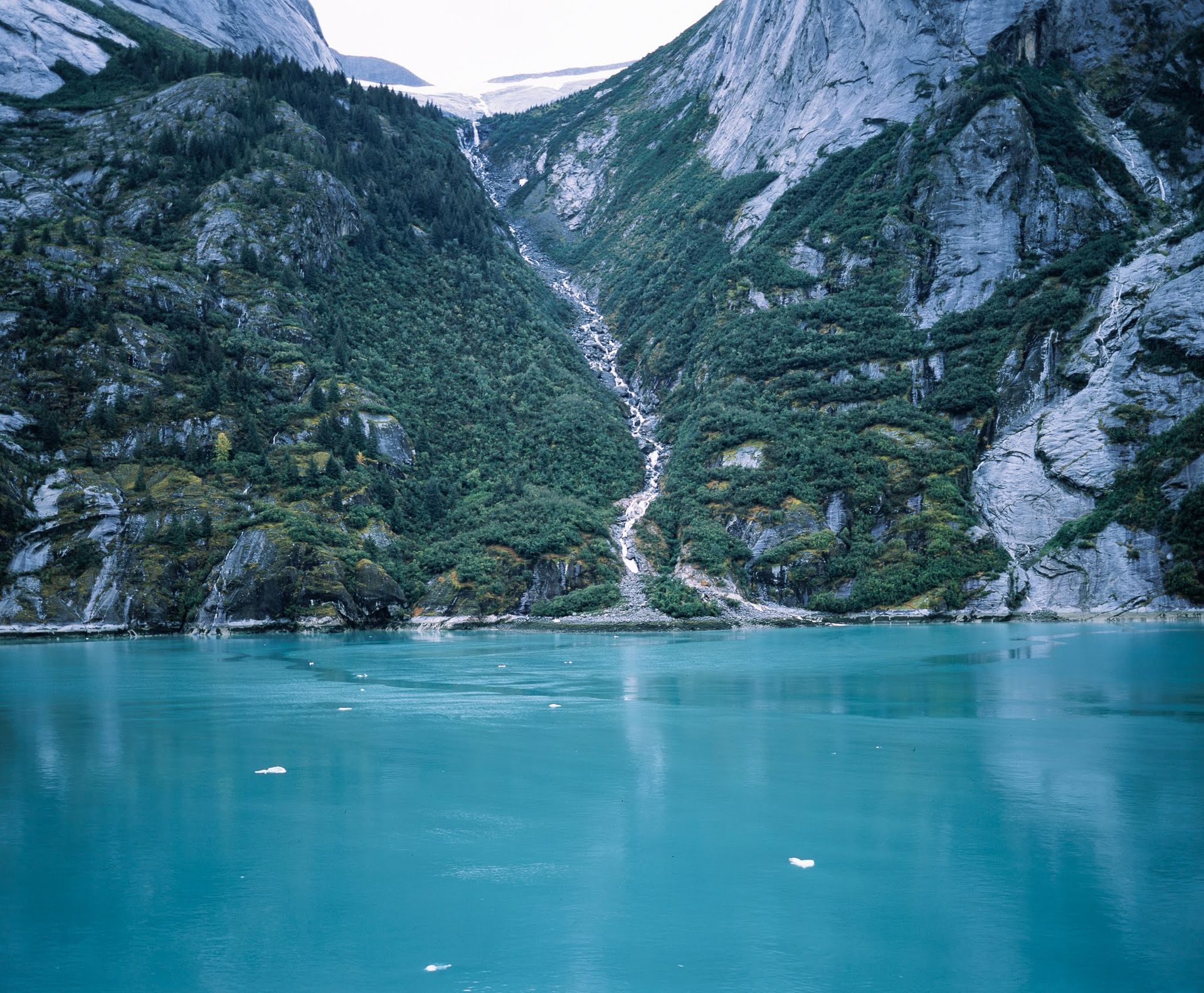 Turquoise lake below steep rocky mountains with a narrow waterfall Turquoise lake below steep rocky mountains with a narrow waterfall