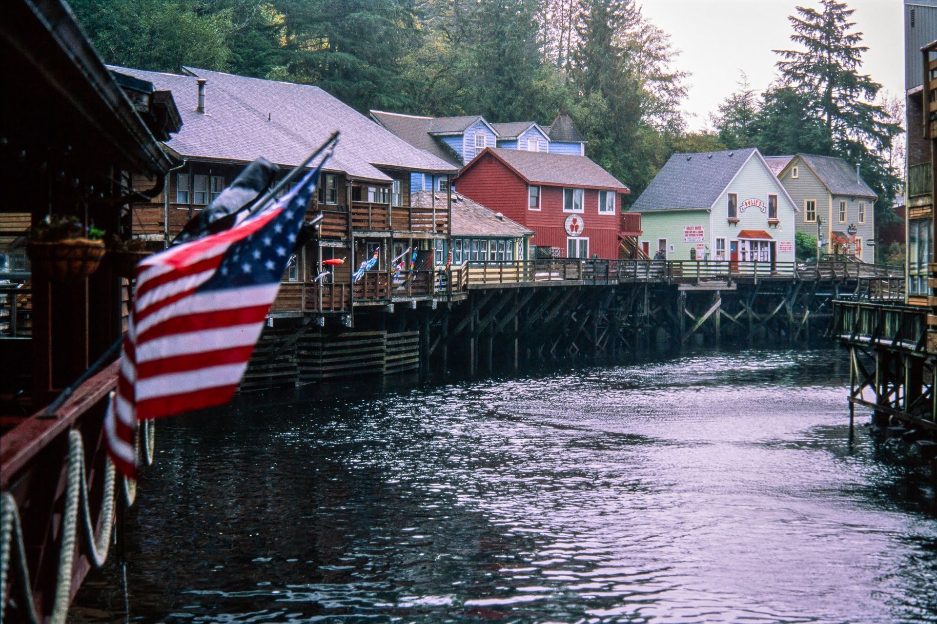 American flag on a wooden waterfront dock beside colorful buildings over calm water American flag on a wooden waterfront dock beside colorful buildings over calm water