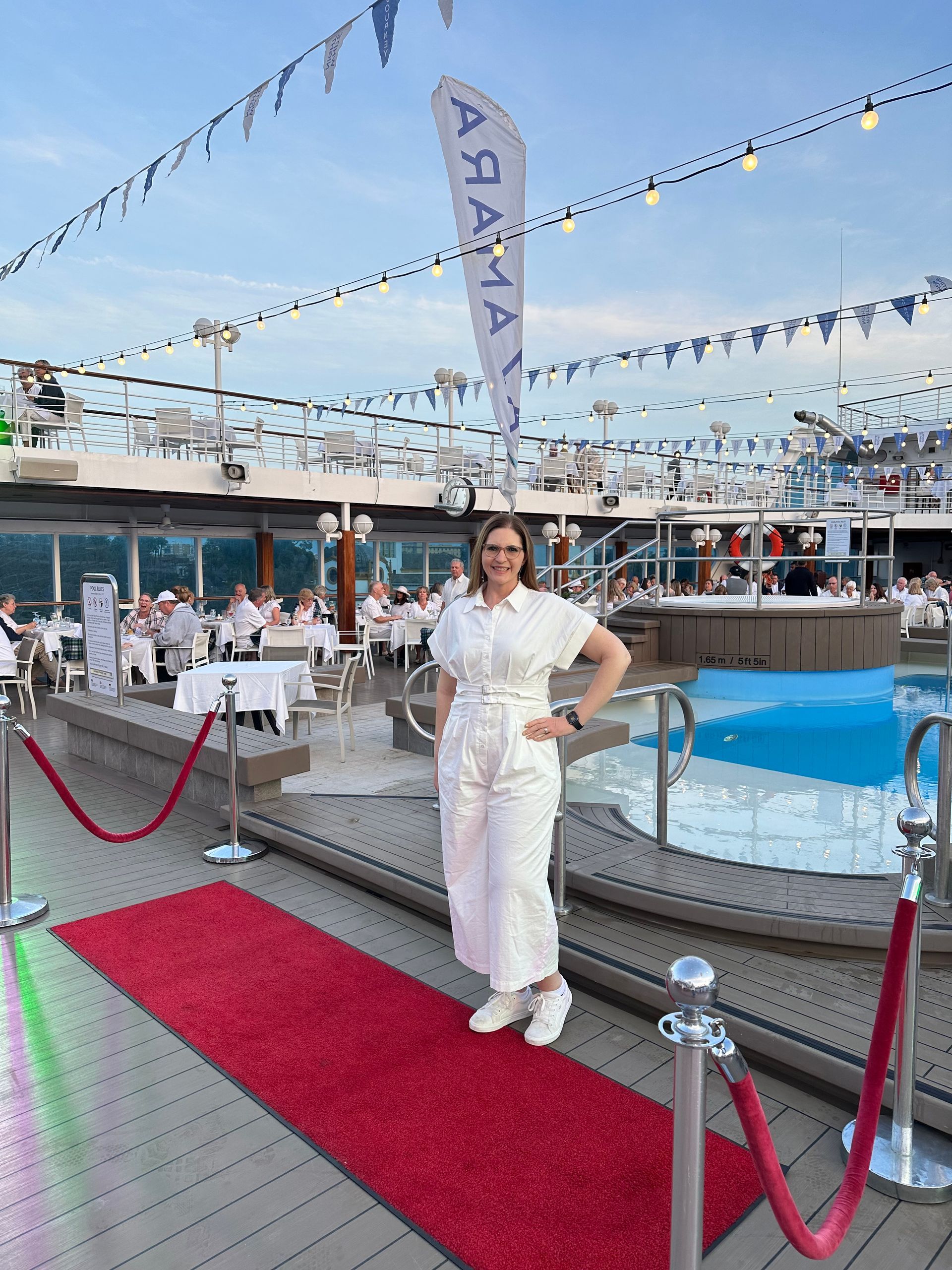 Woman in white outfit stands on red carpet on cruise ship deck. Woman in white outfit stands on red carpet on cruise ship deck.