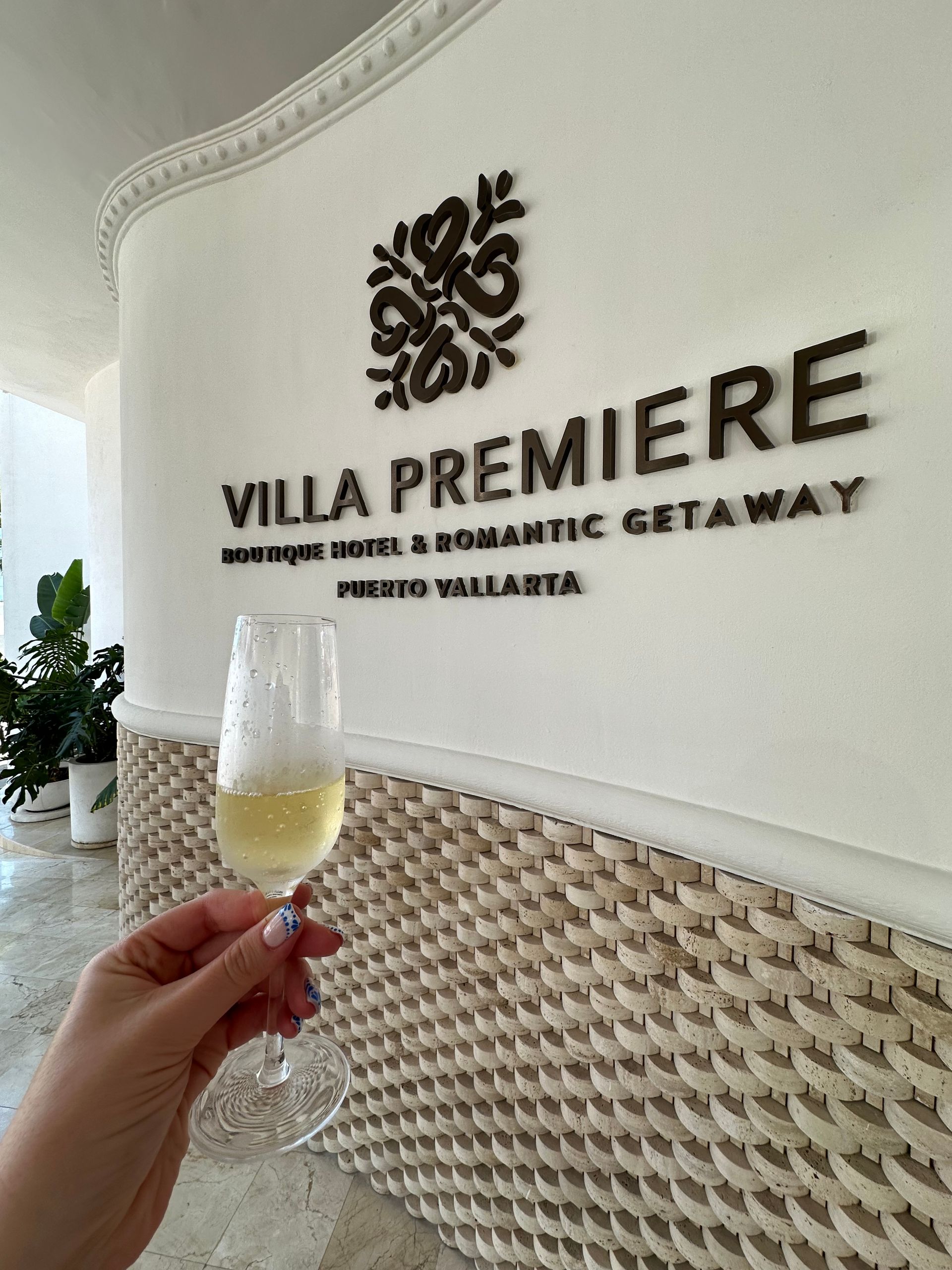 Hand holding a champagne flute in front of the Villa Premiere resort sign and textured wall