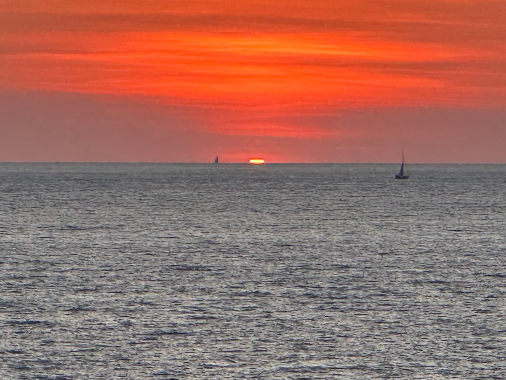 Orange sunset over the ocean with a small sailboat on the horizon Orange sunset over the ocean with a small sailboat on the horizon