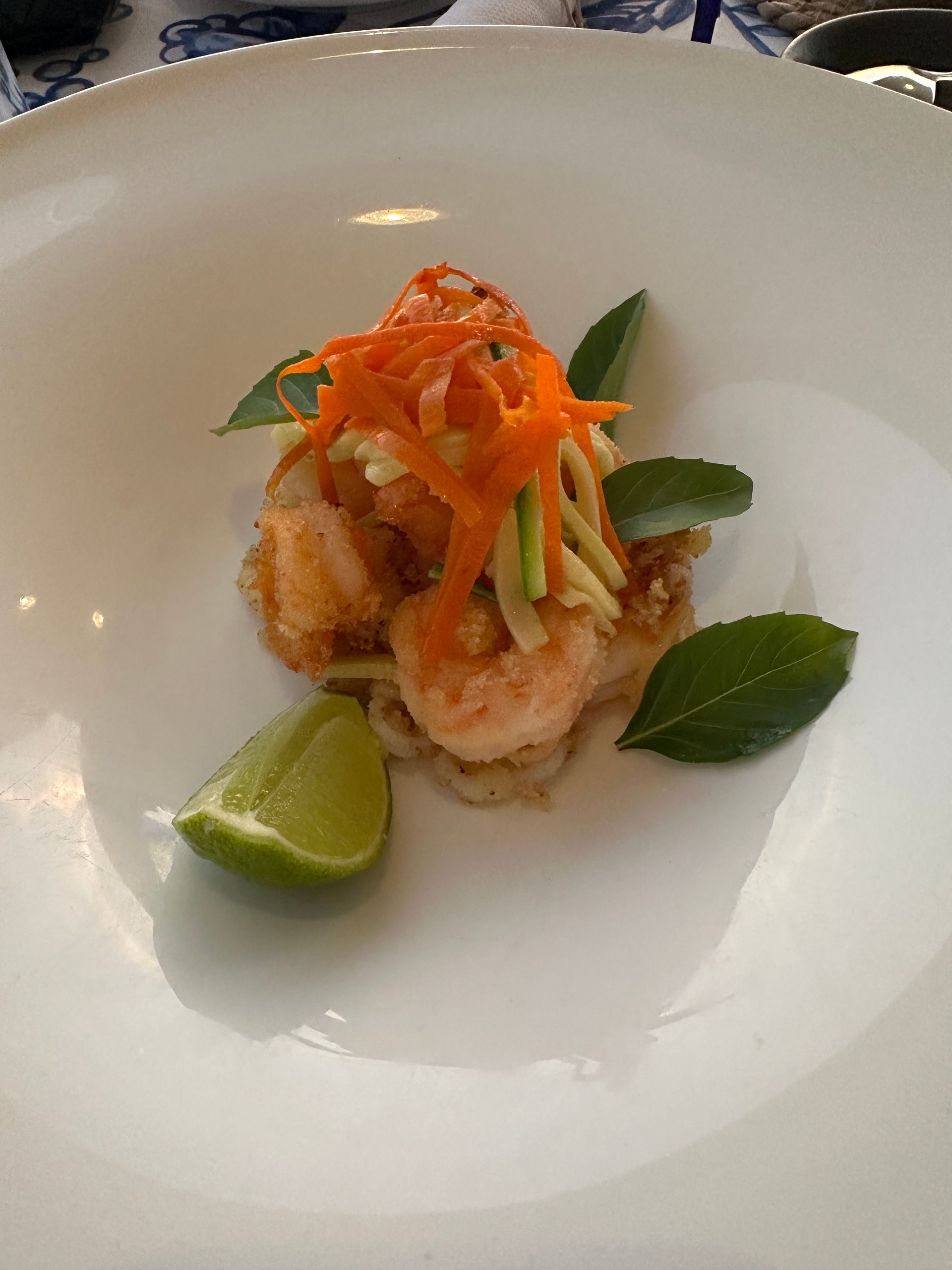 Plated shrimp appetizer topped with shredded carrots and basil, served with a lime wedge on a white plate