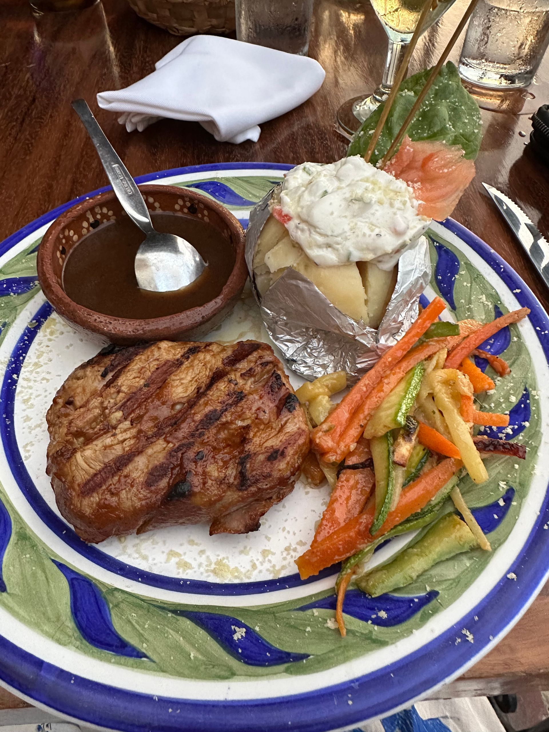 Grilled steak dinner with rice, vegetables, sauce, and a baked potato on a patterned plate