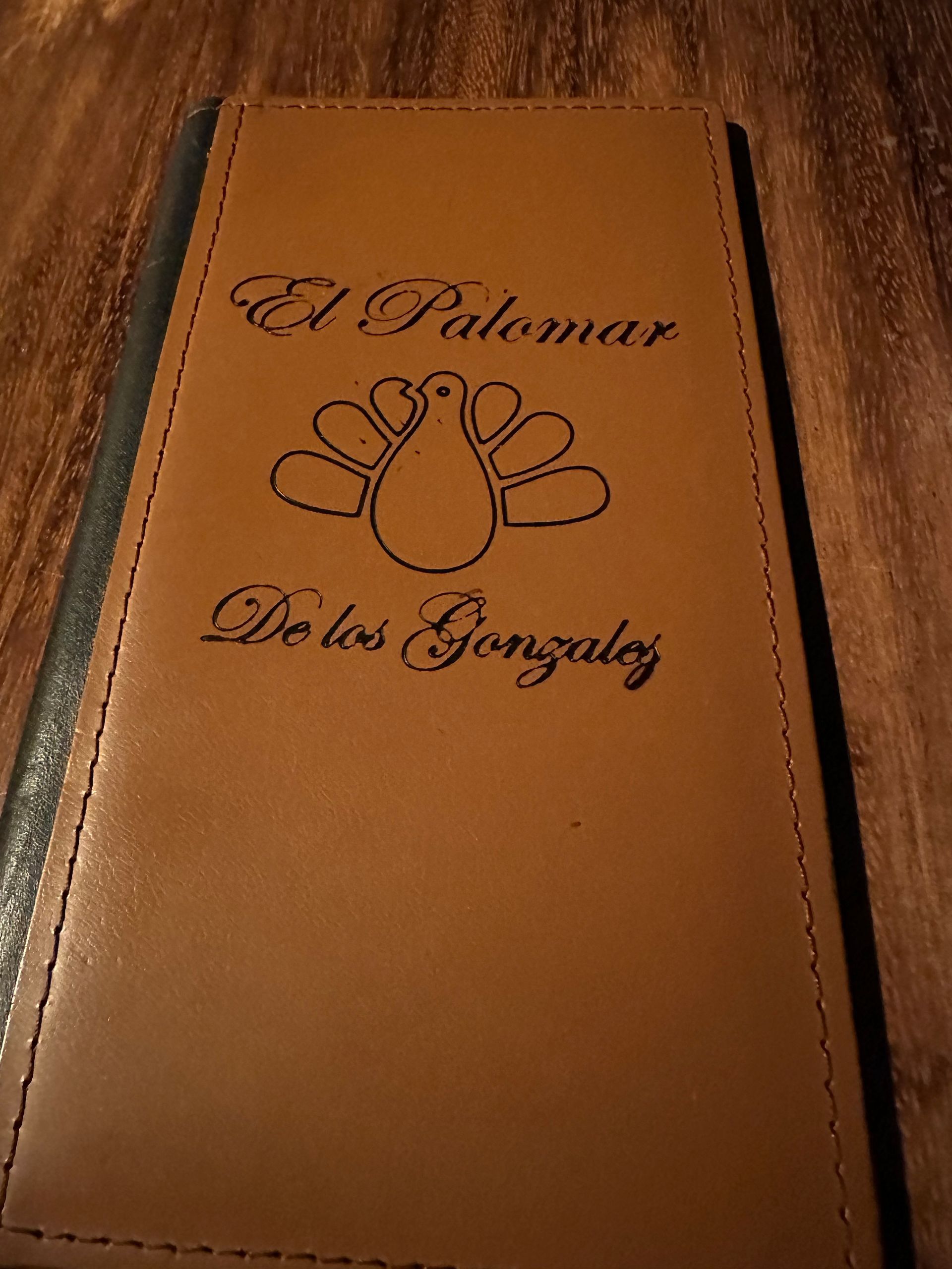 Brown leather-bound menu or book with embossed paw print and cursive text on a wooden surface