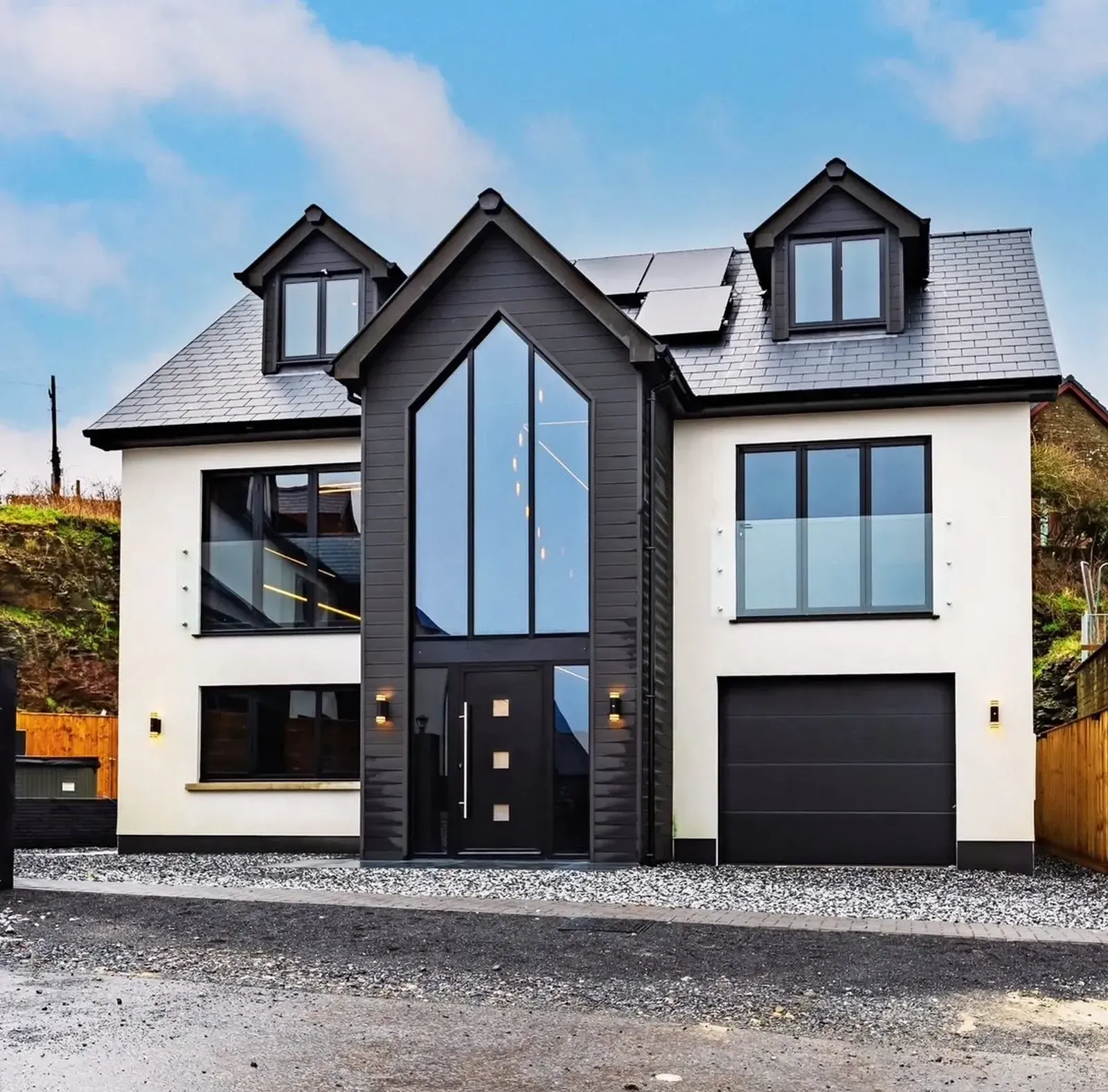 A modern two-story house with a central dark-paneled entrance, floor-to-ceiling windows, and white walls under a blue sky.