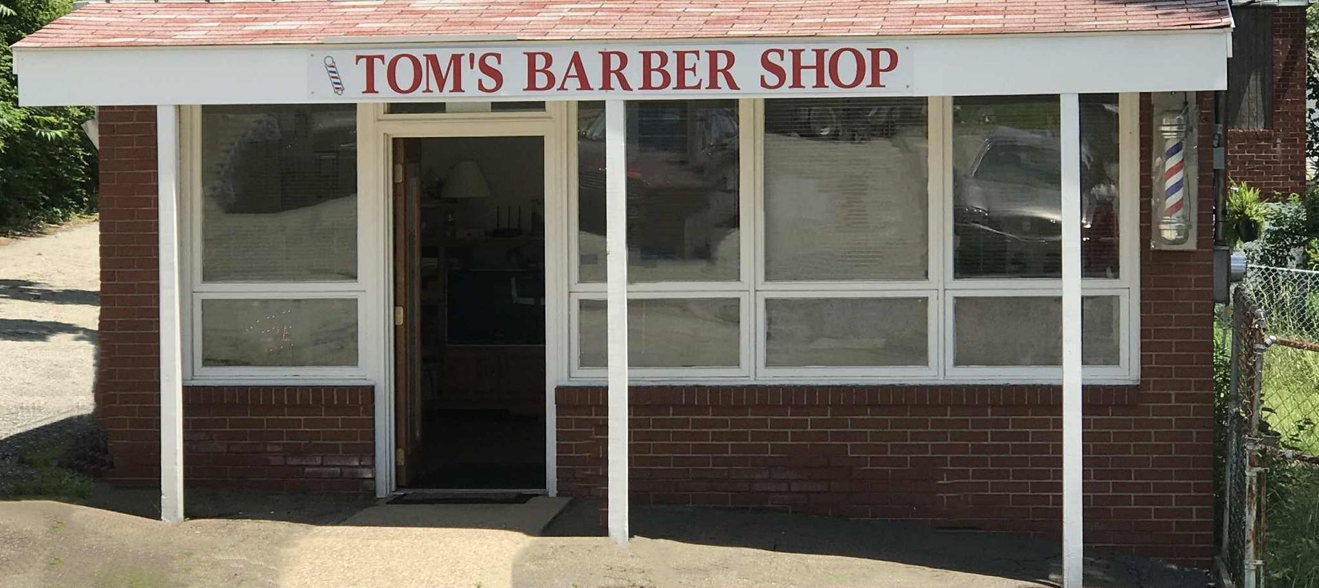 Tom's Barber Shop, a small brick building with a red roof and white trim. Sign reads 