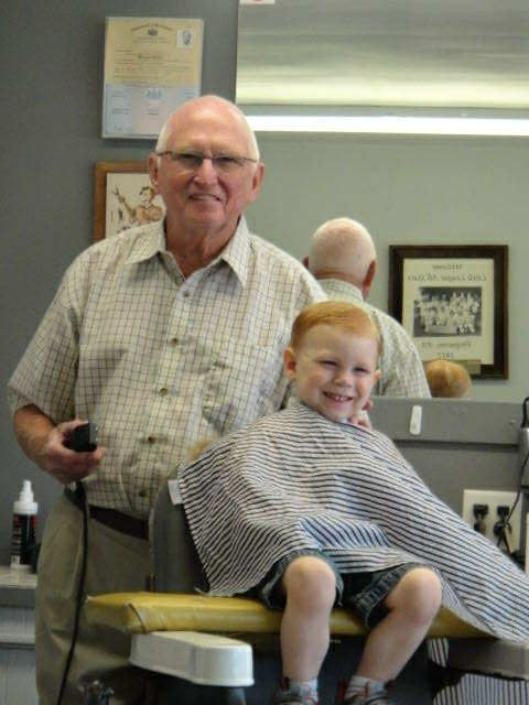Barber giving a haircut to a smiling young boy in a barber shop.