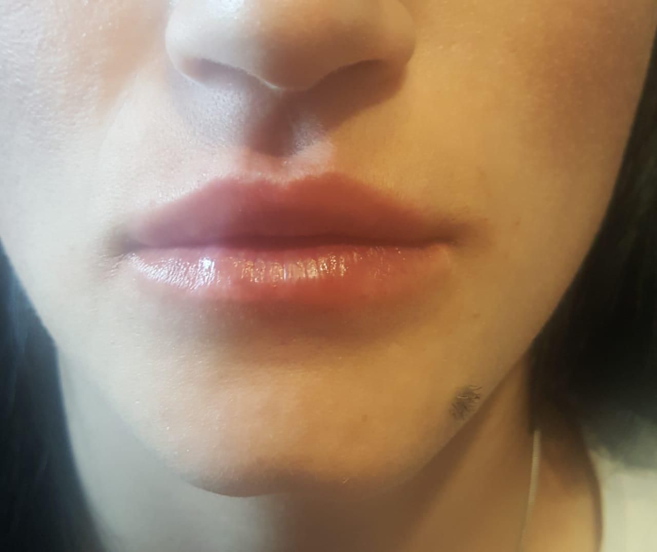 Close-up of a person's lips. They are full, glossy, and light pink in color.