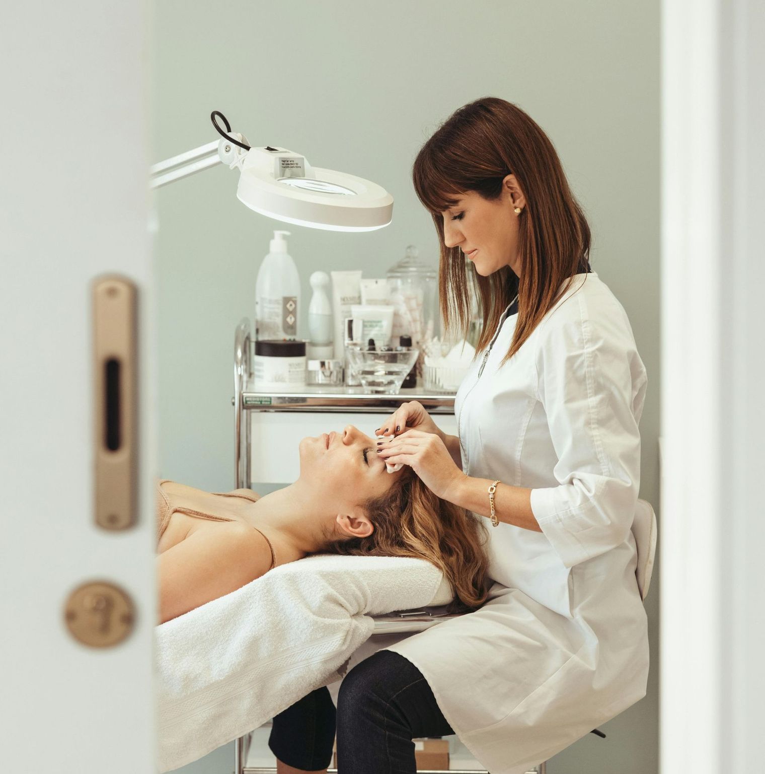 Woman giving facial to a client in a spa. Both are fair skinned.
