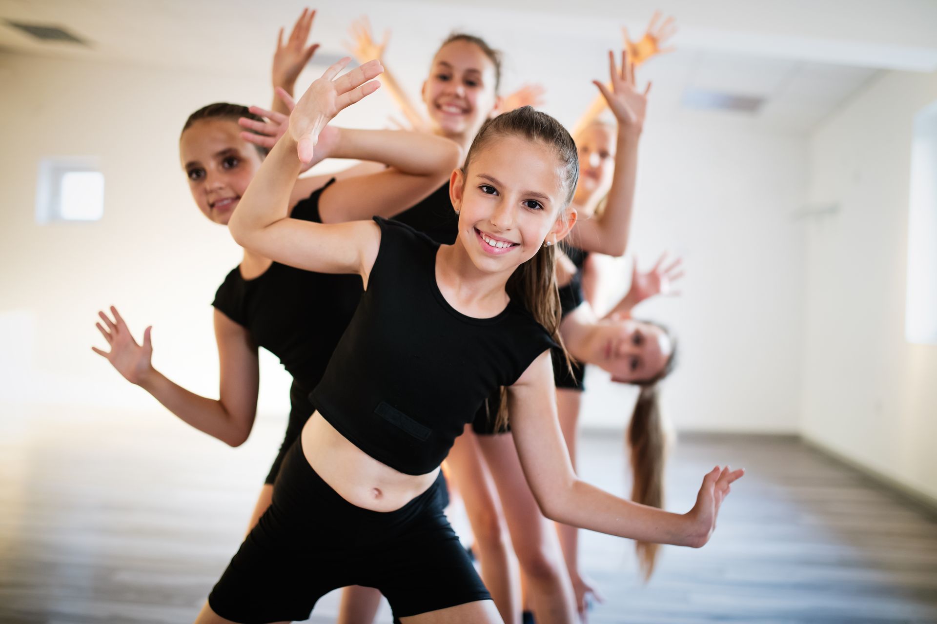 Young dancers in black outfits posing and smiling in a dance studio.