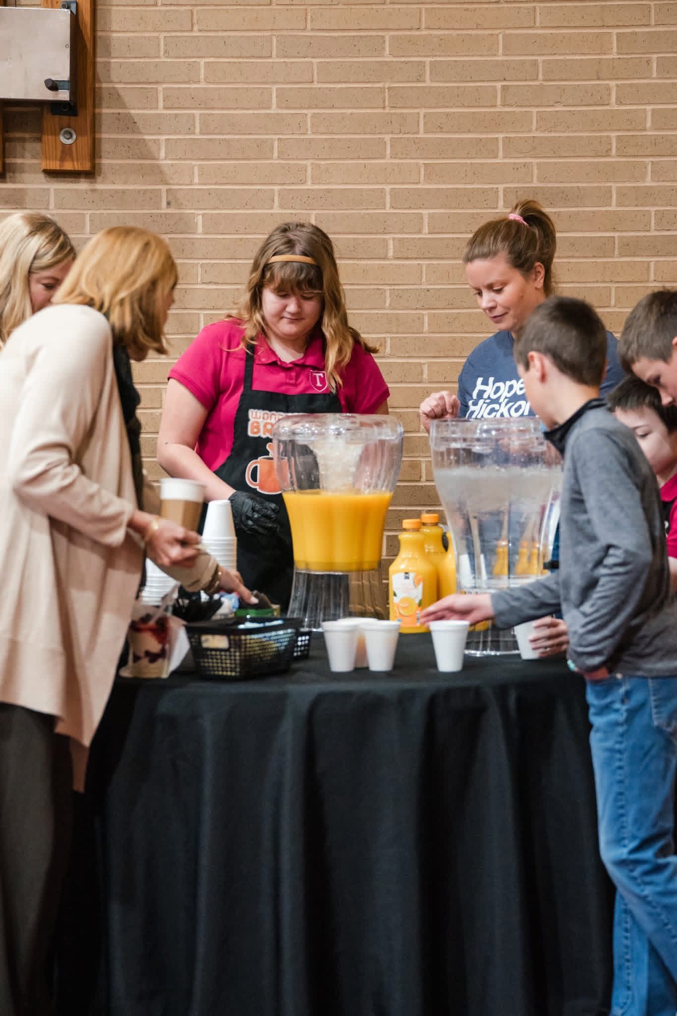 People serving drinks at a refreshment table with cups and pitchers in a brick-walled room