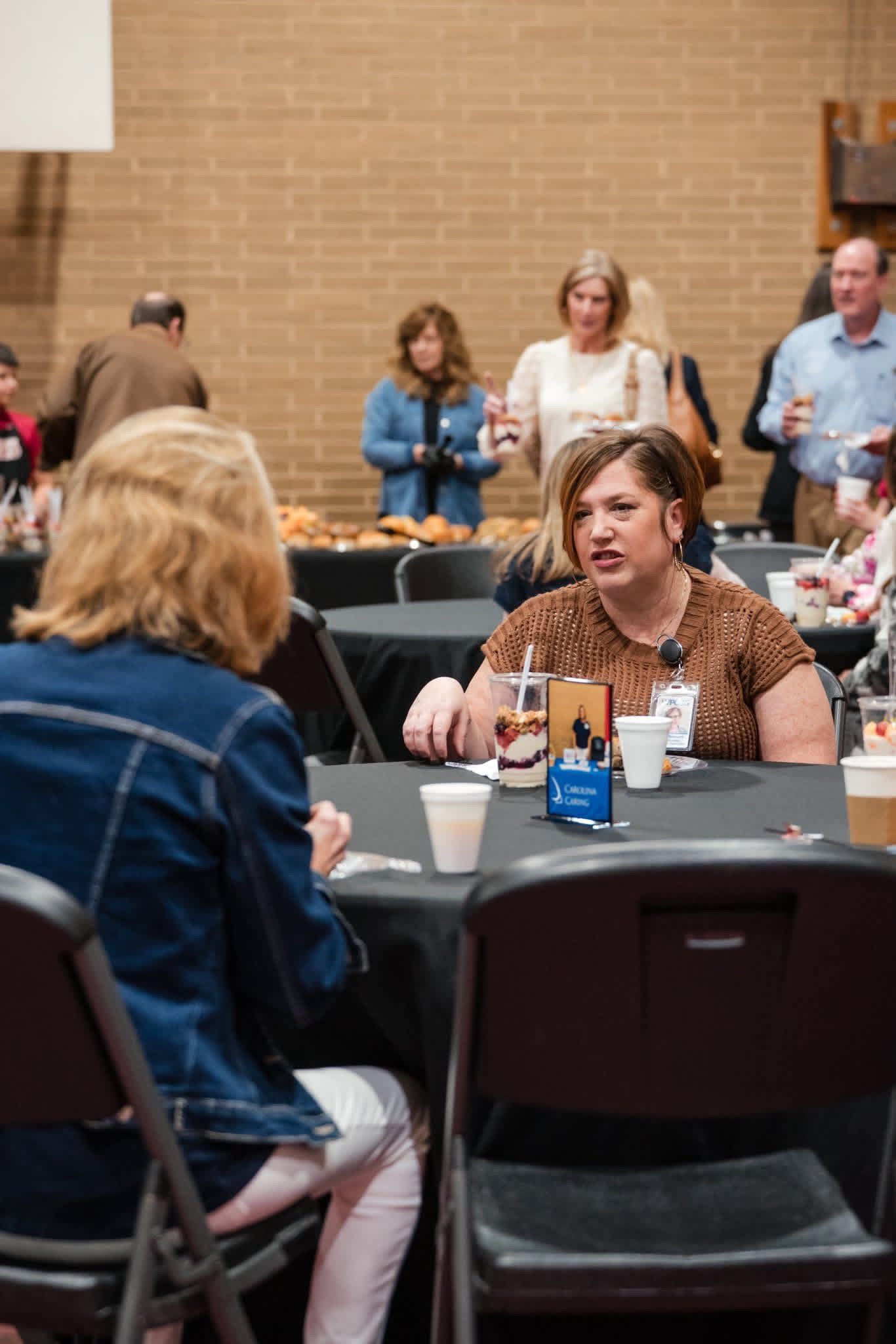 People seated at round tables in a meeting room, with drinks and conversation.