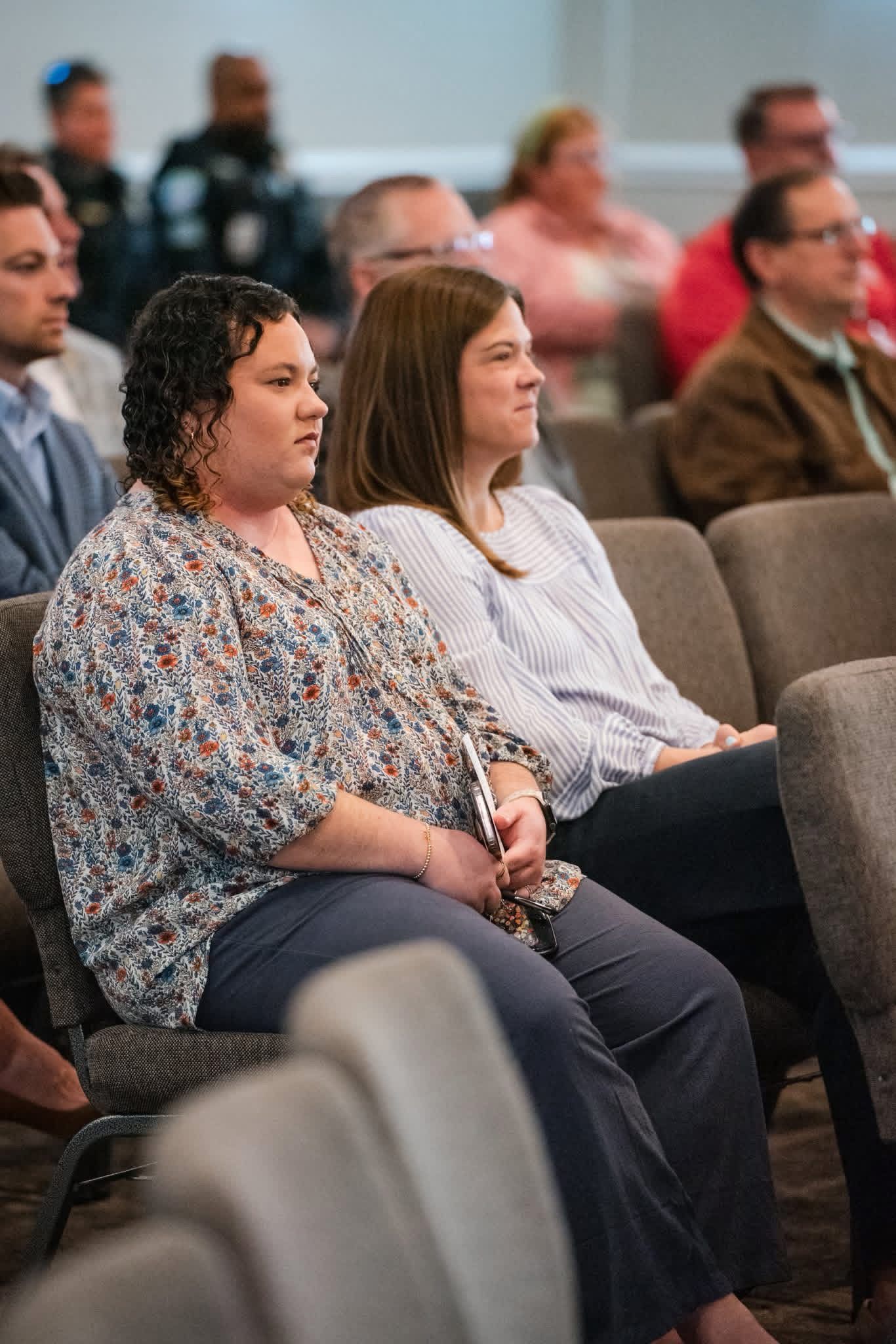 Audience seated in rows at a conference, with two women in the foreground listening attentively.