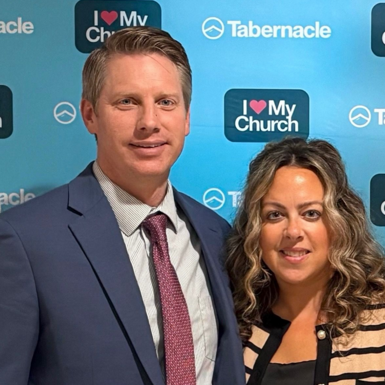 Two people posing at a Tabernacle event with an “I ♥ My Church” backdrop