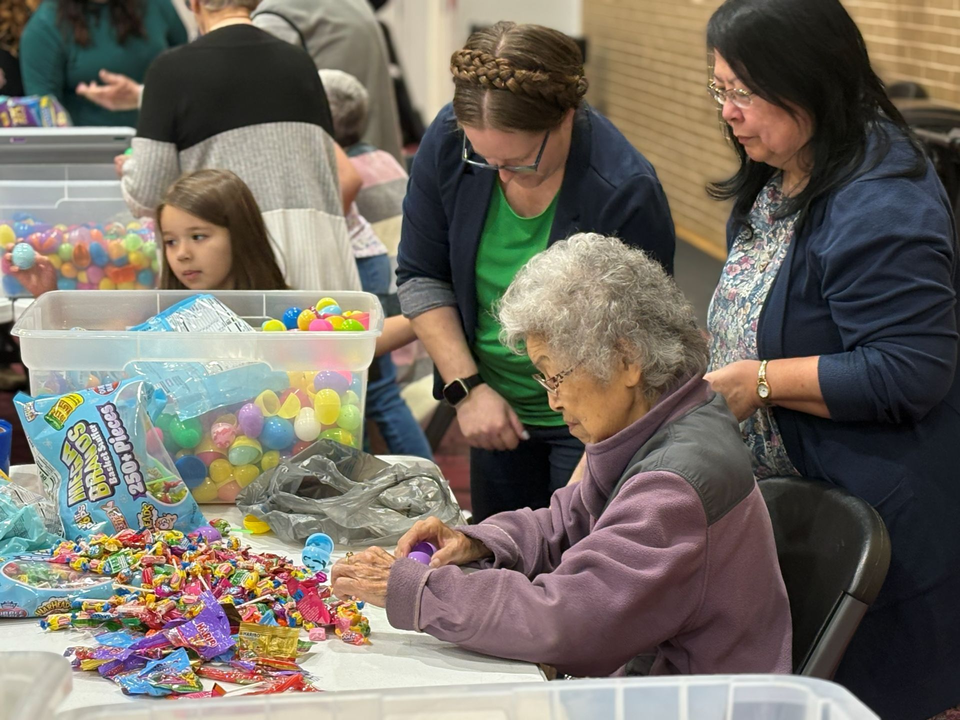 People at a table making colorful craft projects with bins of beads and supplies