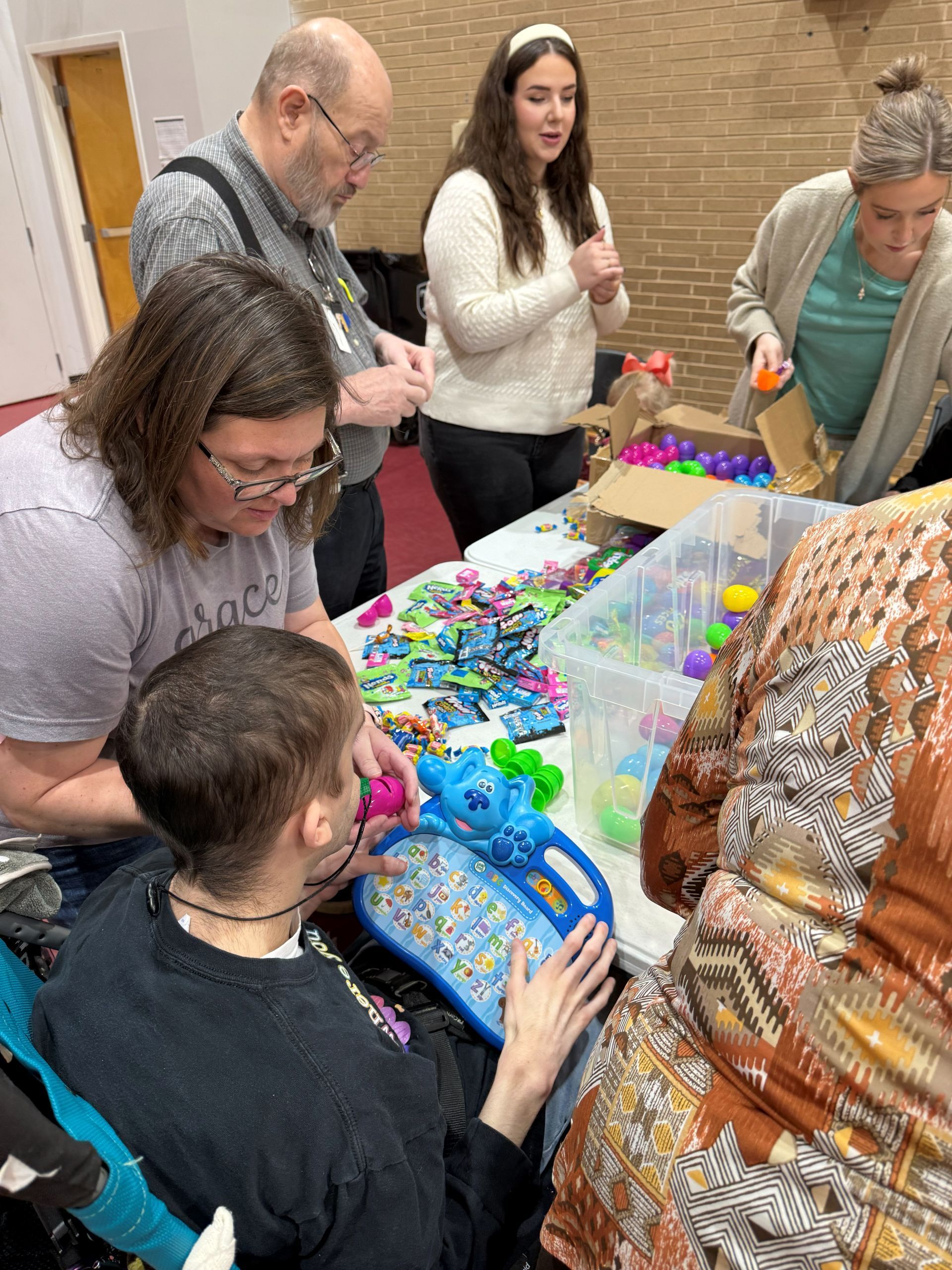 People gathered around a colorful table of craft materials, working together in a bright room.
