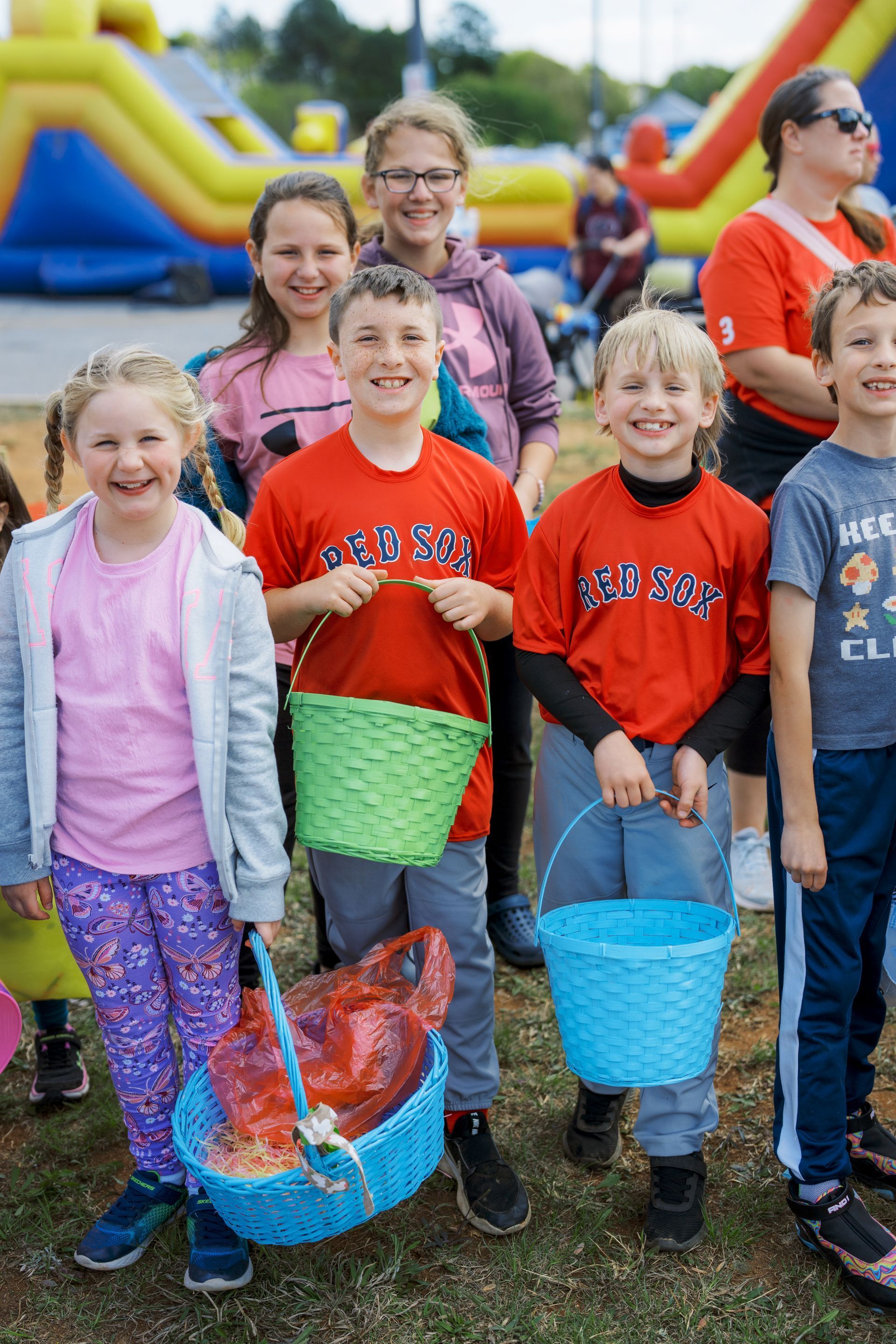 Children holding colorful buckets at an outdoor event with inflatable slides in the background
